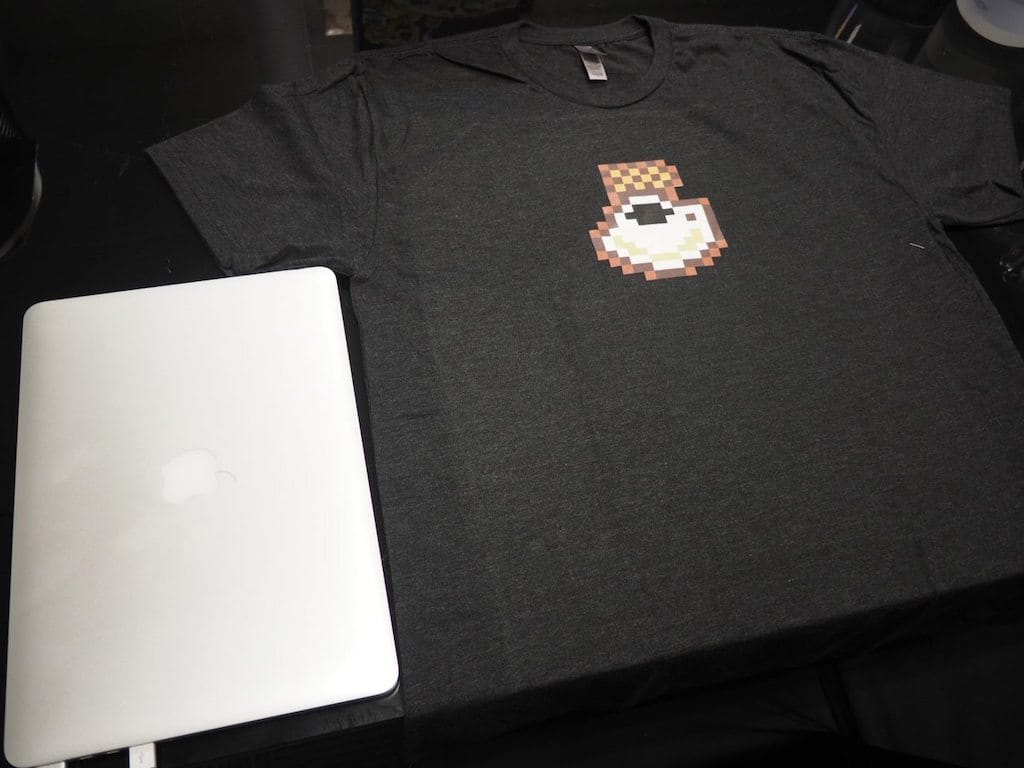 The pixelated KopiJS t-shirt, besides a Macbook for size comparison